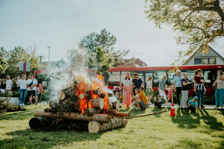 A lively community gathering enjoying a bonfire event outdoors on a sunny day.
